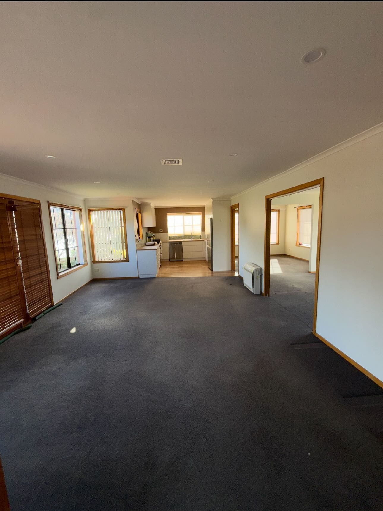 Spacious room with dark carpet, doorway to kitchen, windows on the left side, and doorway to another room on the right.