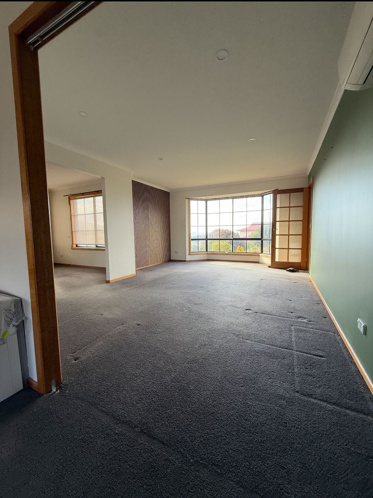 Empty living room with dark gray carpet, green and patterned accent walls, and large windows.