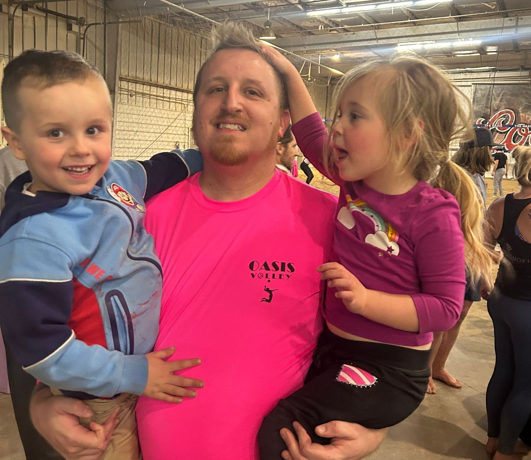 A man in a pink shirt is holding two children.
