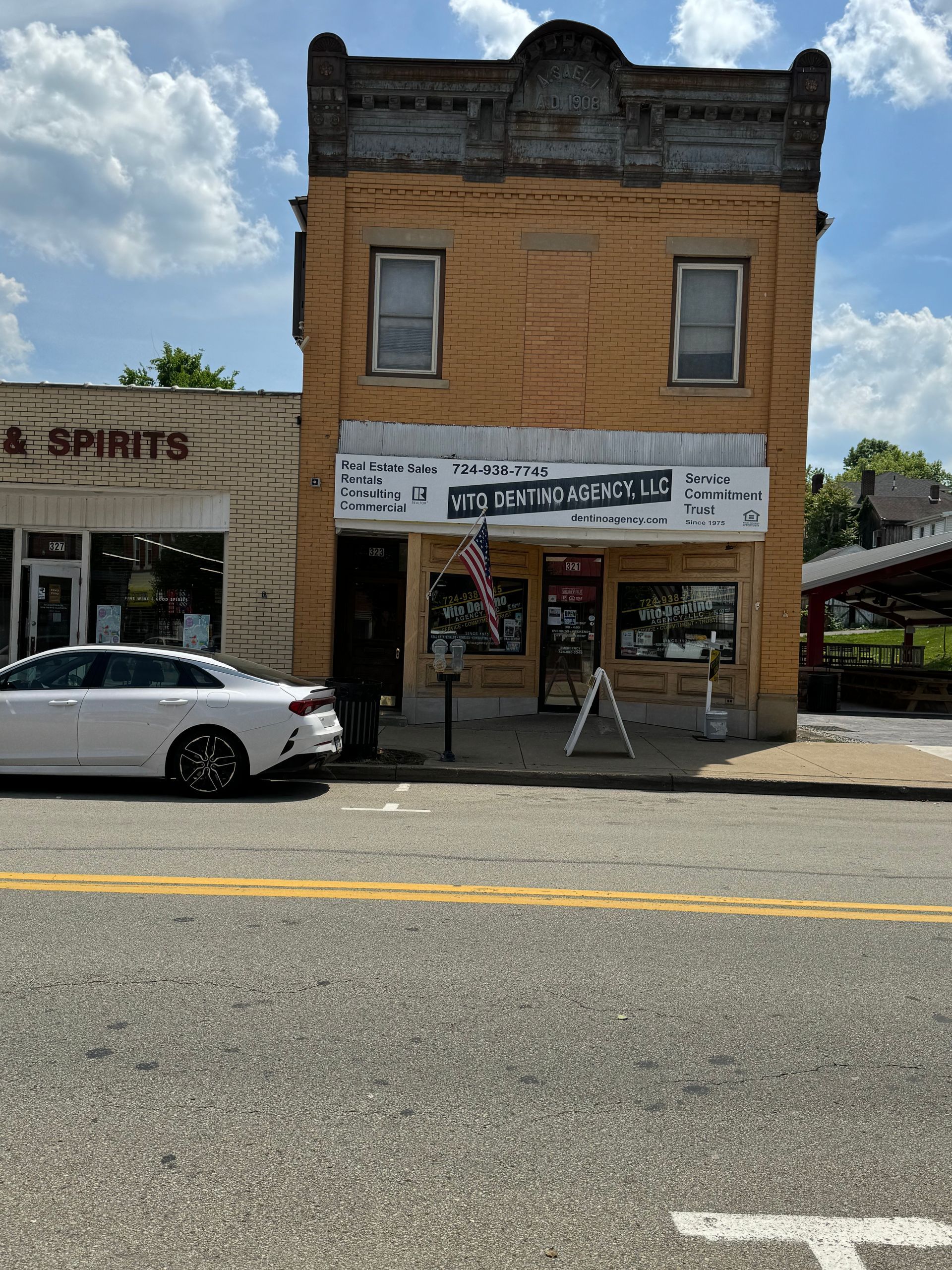 A white car is parked in front of a building that says spirits