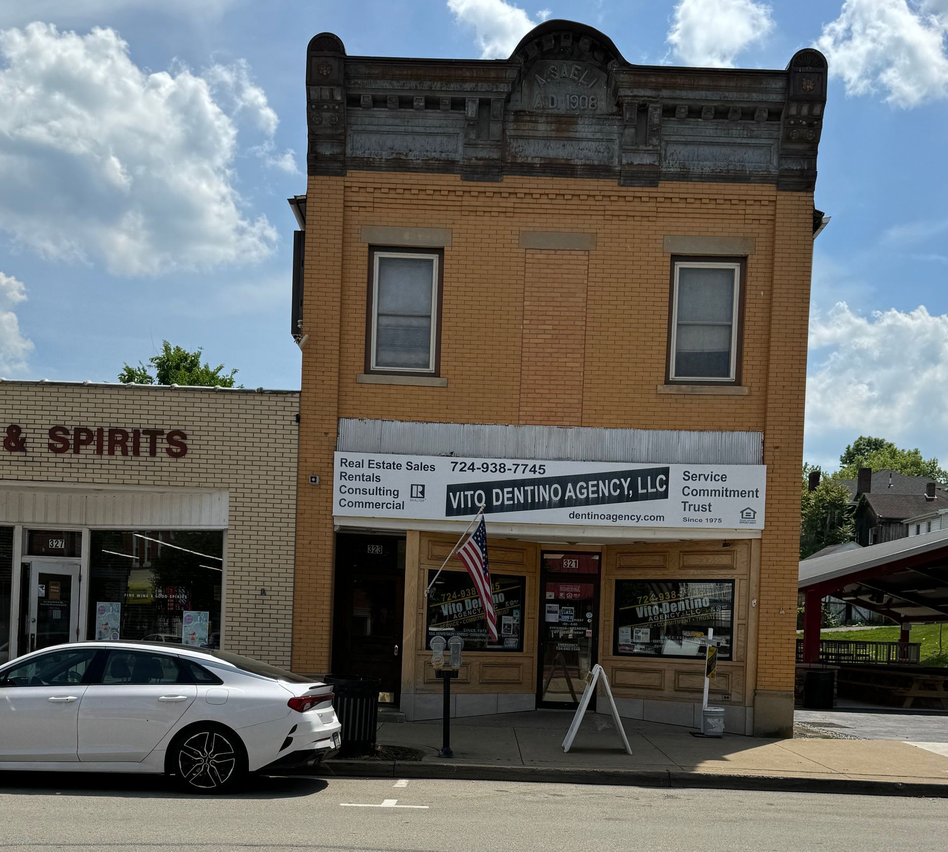 A white car is parked in front of a building that says spirits