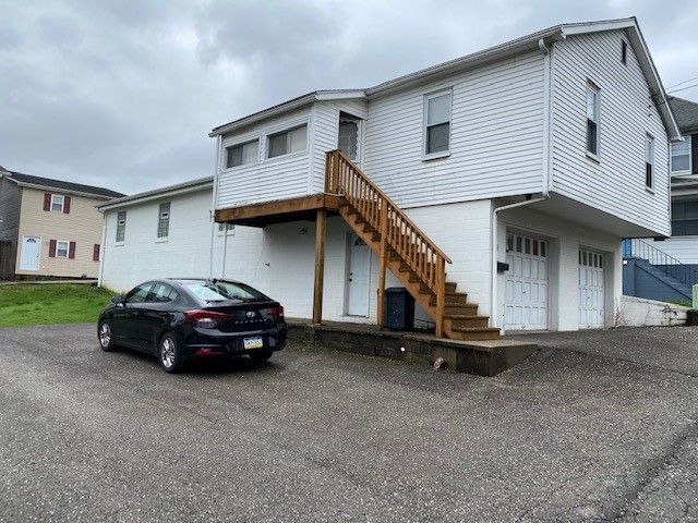 A black car is parked in front of a white house with stairs.