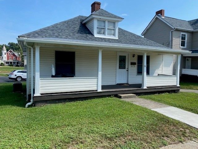 A small white house with a porch and a car parked in front of it.
