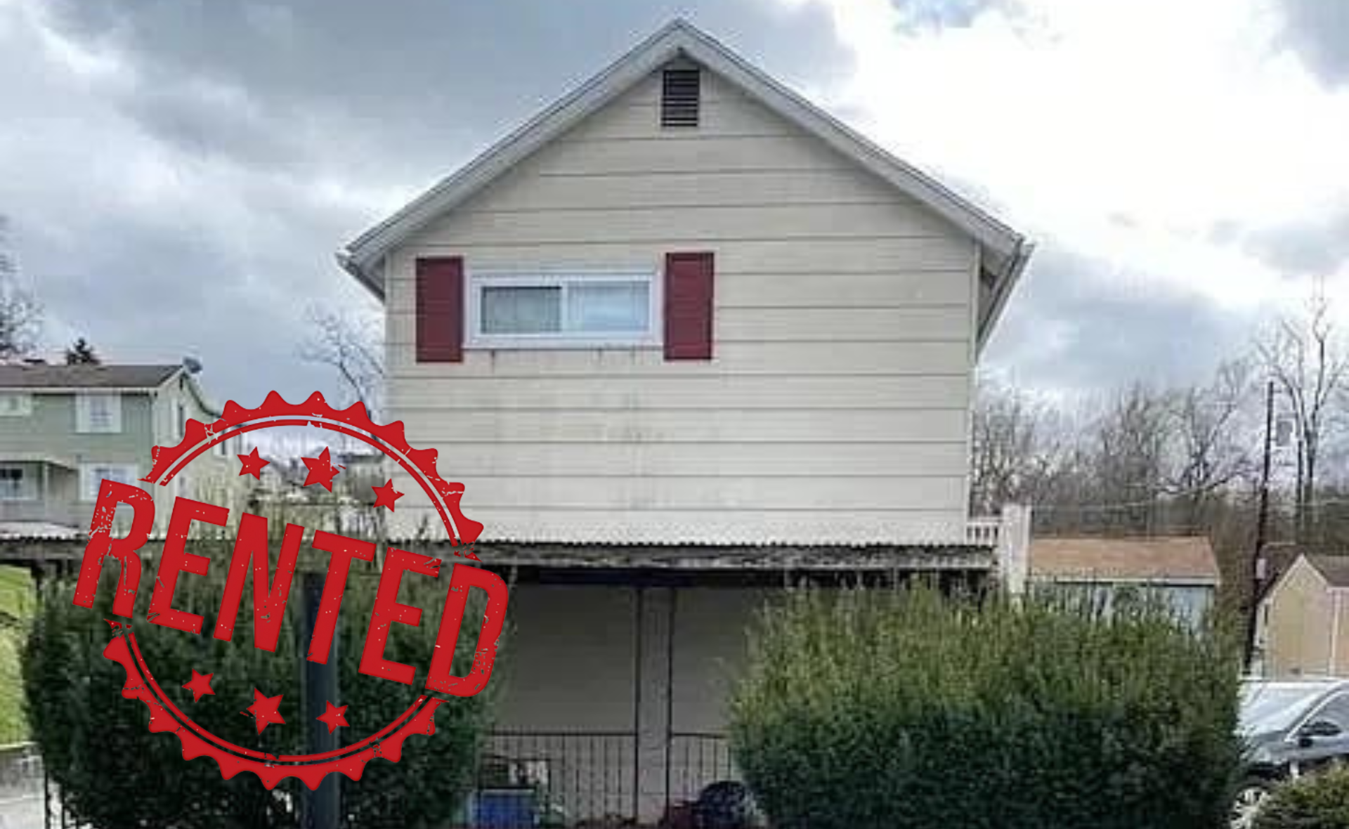 A small white house with red shutters is sitting on top of a lush green lawn.