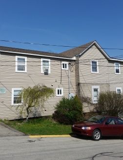 A red car is parked in front of a large house