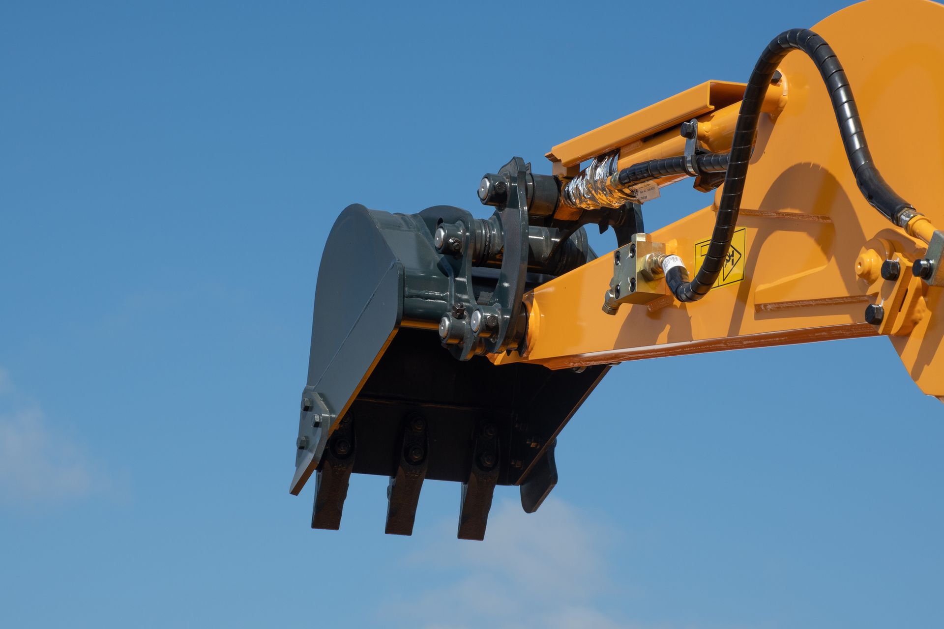 Close-up of a yellow and black excavator bucket against a blue sky.