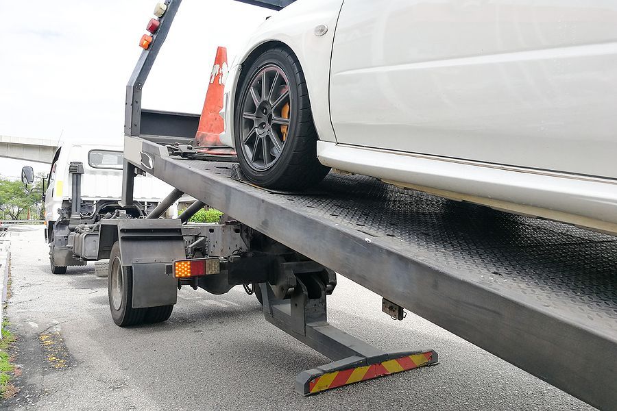 White car on a tow truck ramp, with an orange cone and black wheel lift in a roadside lot
