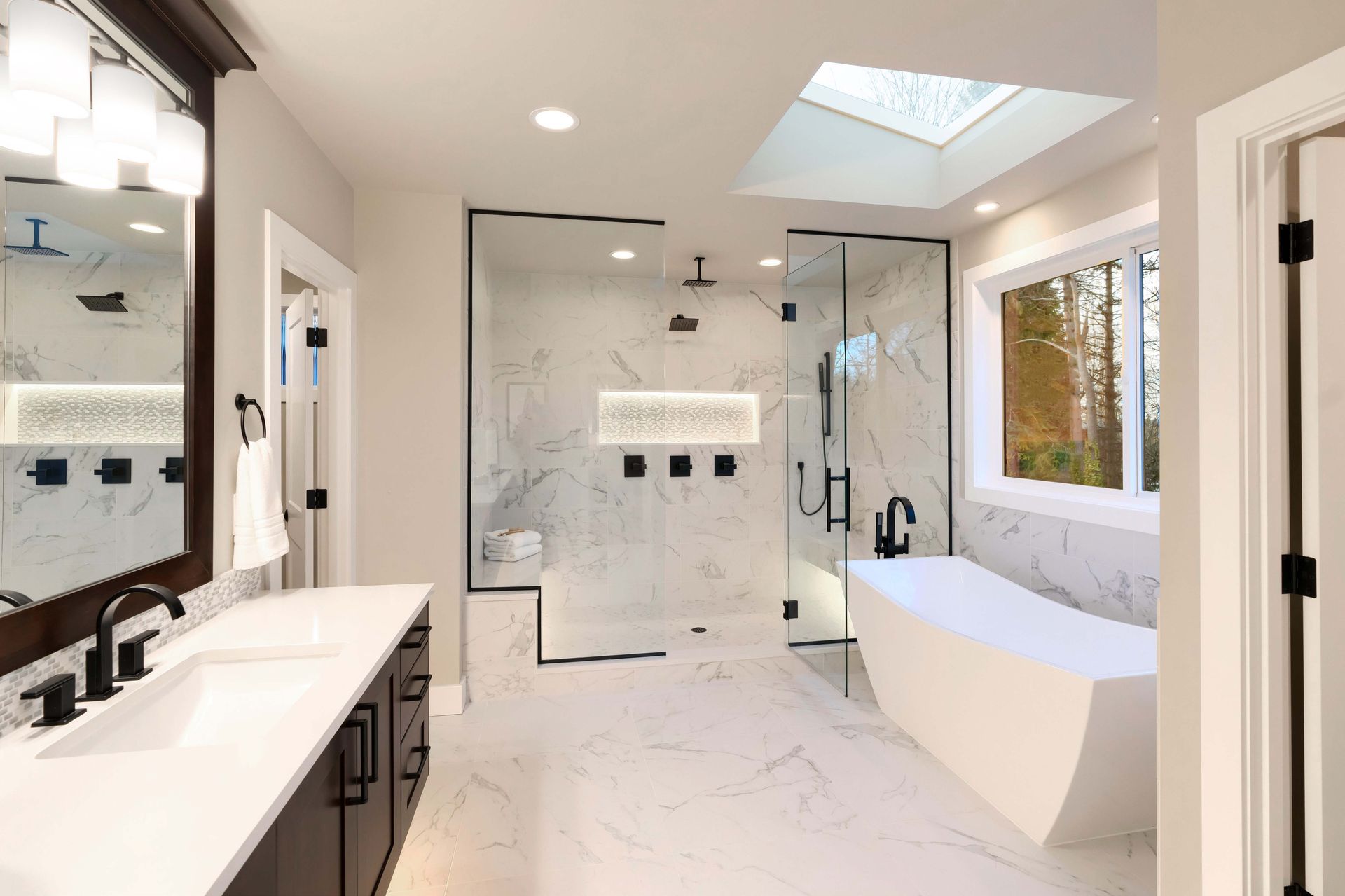 Modern bathroom with marble tile, glass shower, soaking tub, and vanity with black fixtures.
