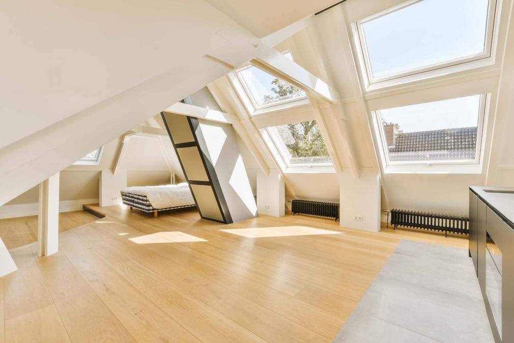 Spacious attic bedroom with angled ceilings, skylight windows, hardwood floors, and a bed.