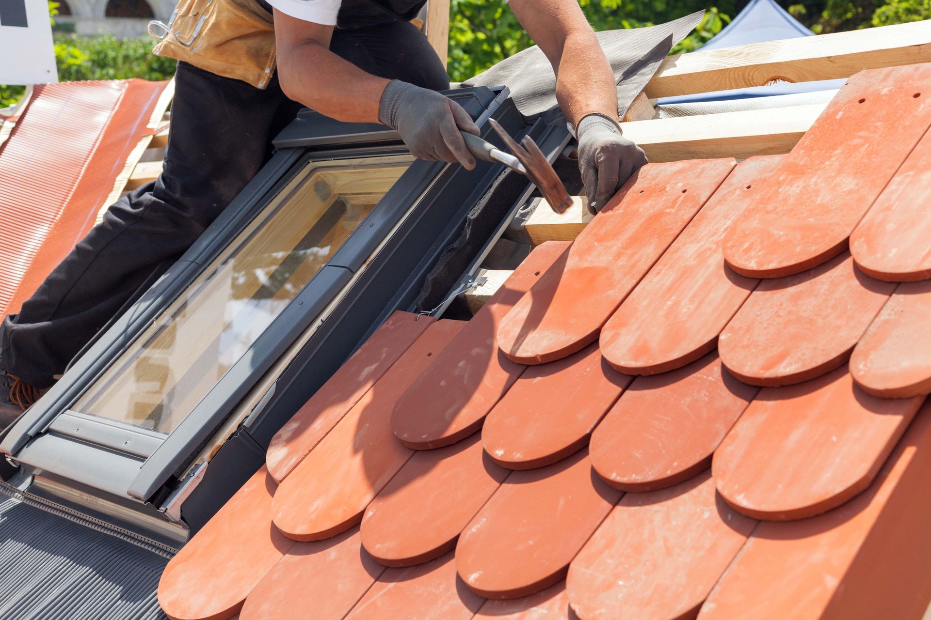 Roofer installing clay tiles around a skylight on a roof; sunny day.