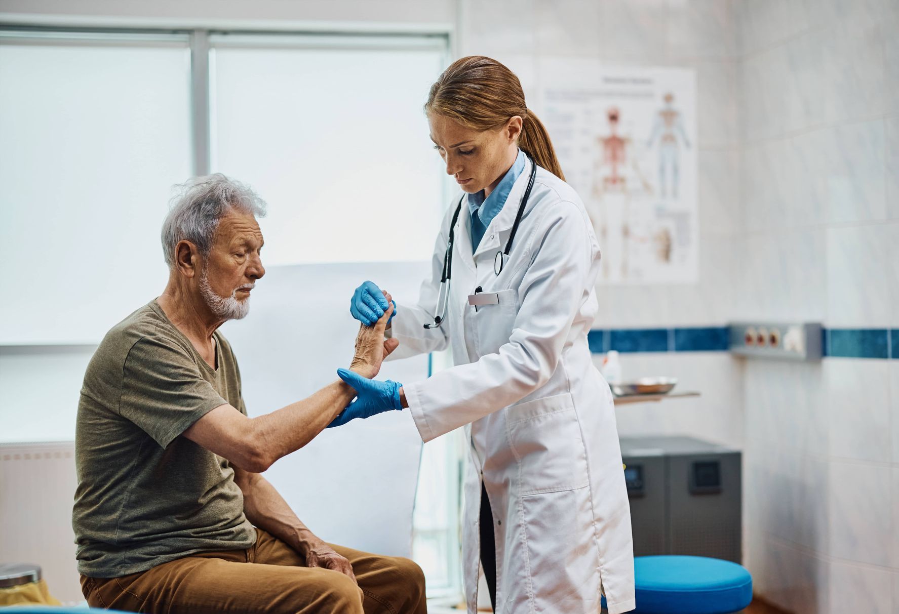 A doctor is examining an older man 's wrist in a hospital.