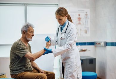 A doctor is examining an older man 's wrist in a hospital.