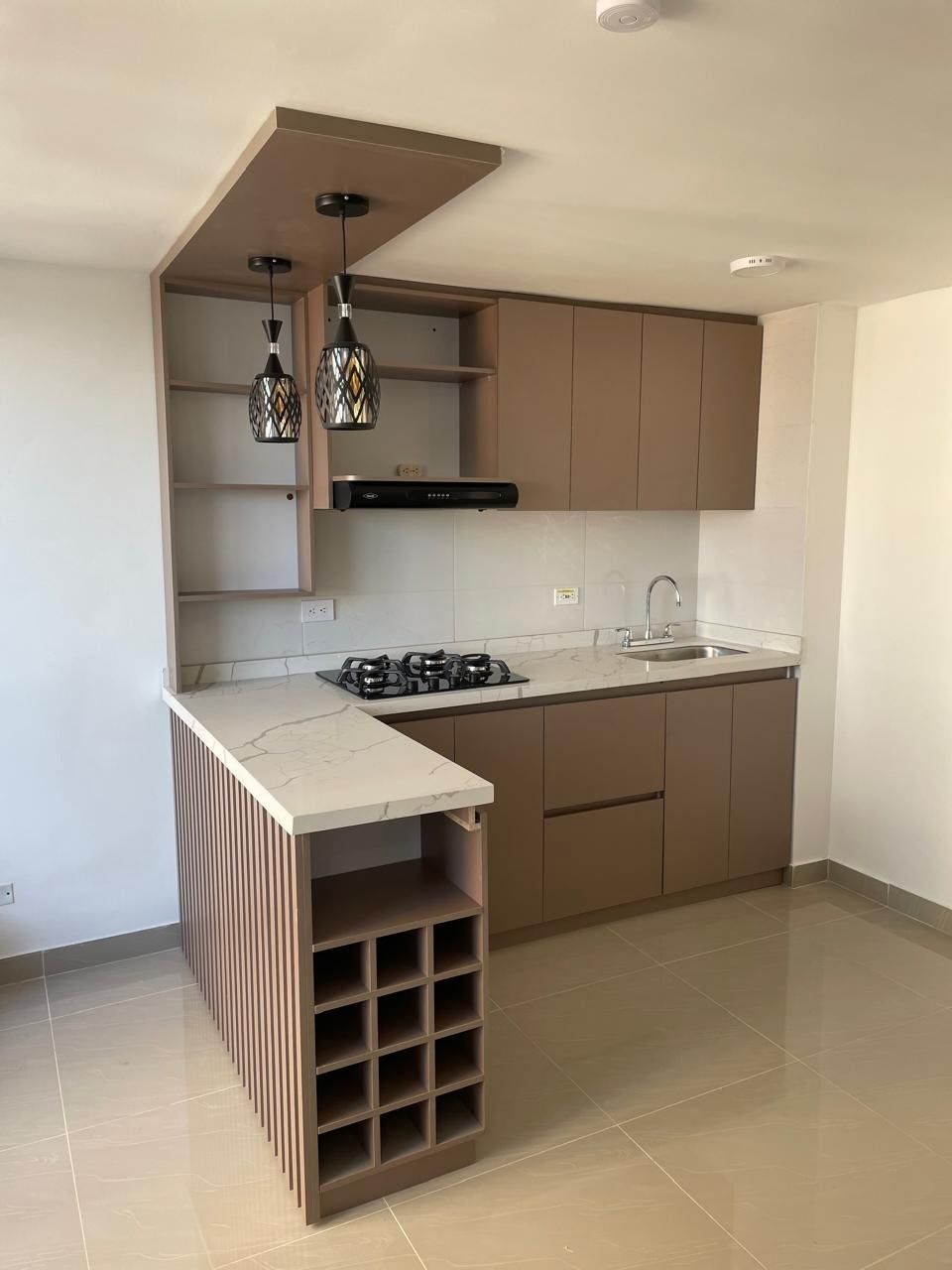 Cocina moderna con gabinetes de color marrón claro, encimeras blancas y un botellero incorporado.