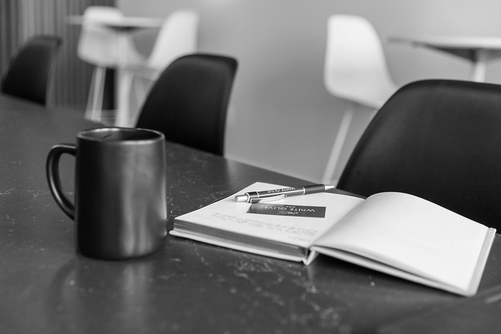 A cup of coffee sits on a table next to an open book