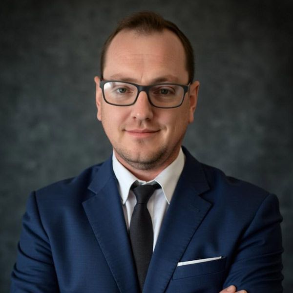 Stephan Barkhuizen of White Olive CPA in a blue suit and tie, arms crossed, against a dark background.