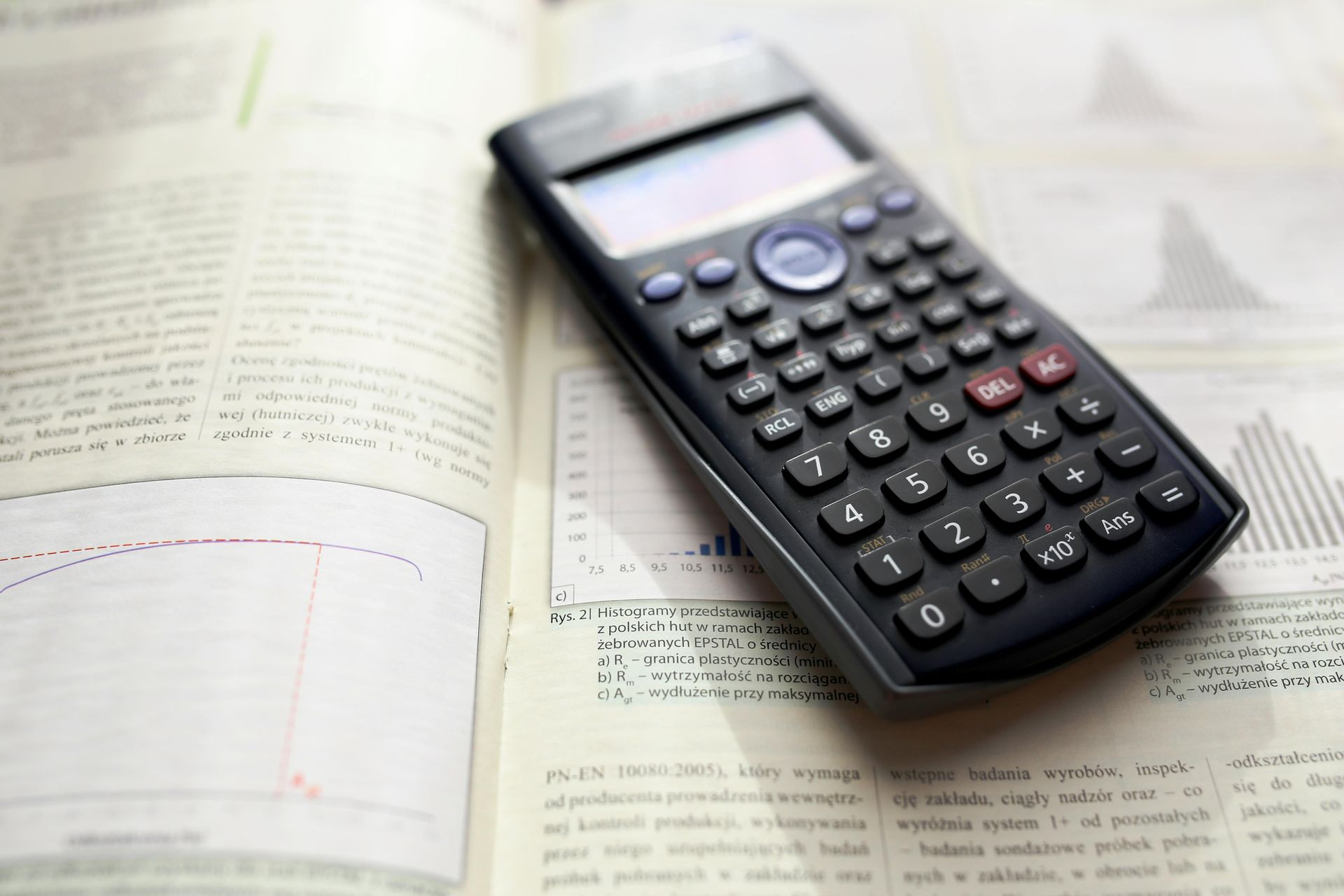Scientific calculator on an open textbook with graphs and text.