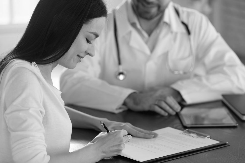 A woman is sitting at a table with a doctor and writing on a clipboard.