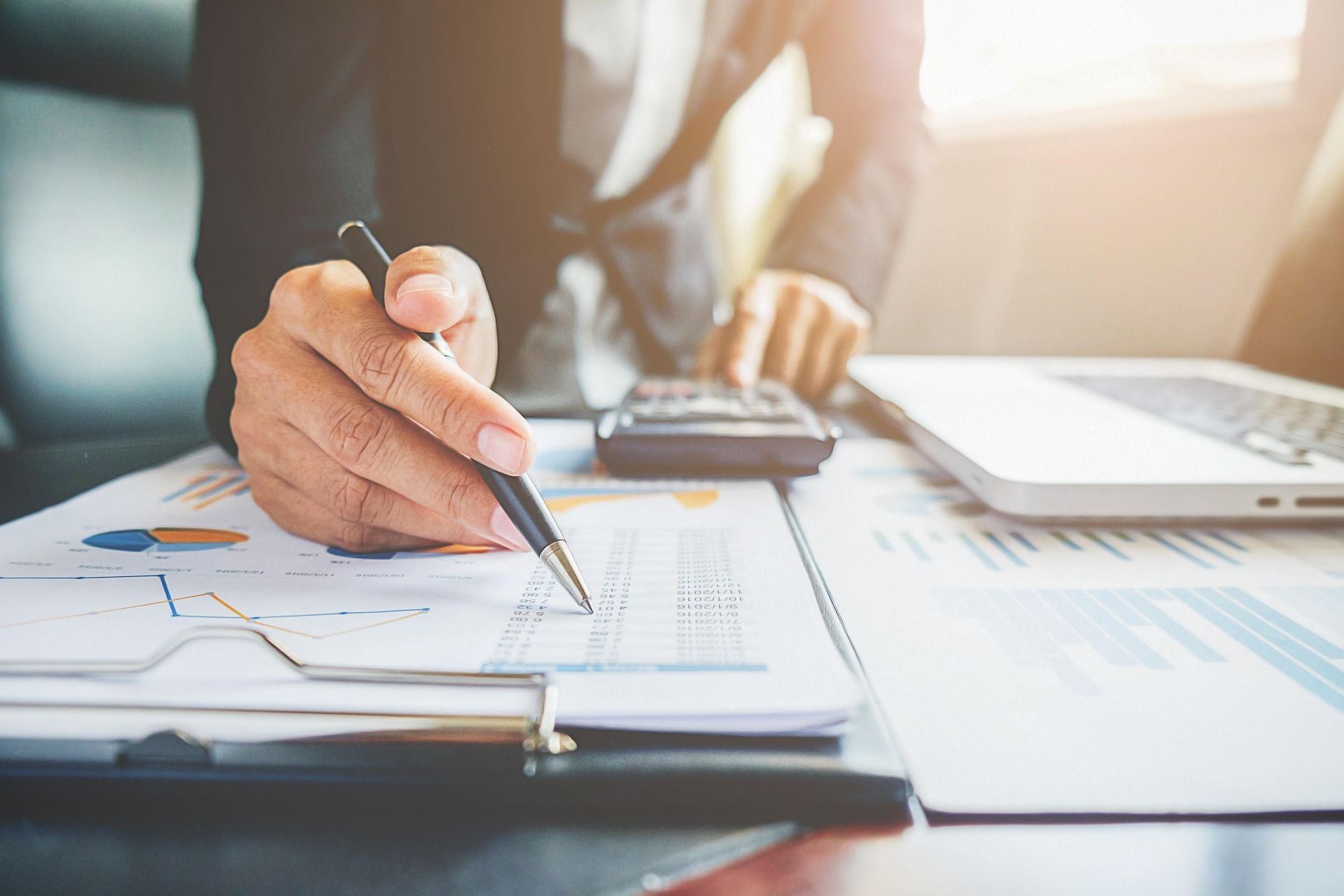 A man is sitting at a desk using a calculator and a pen for tax services.