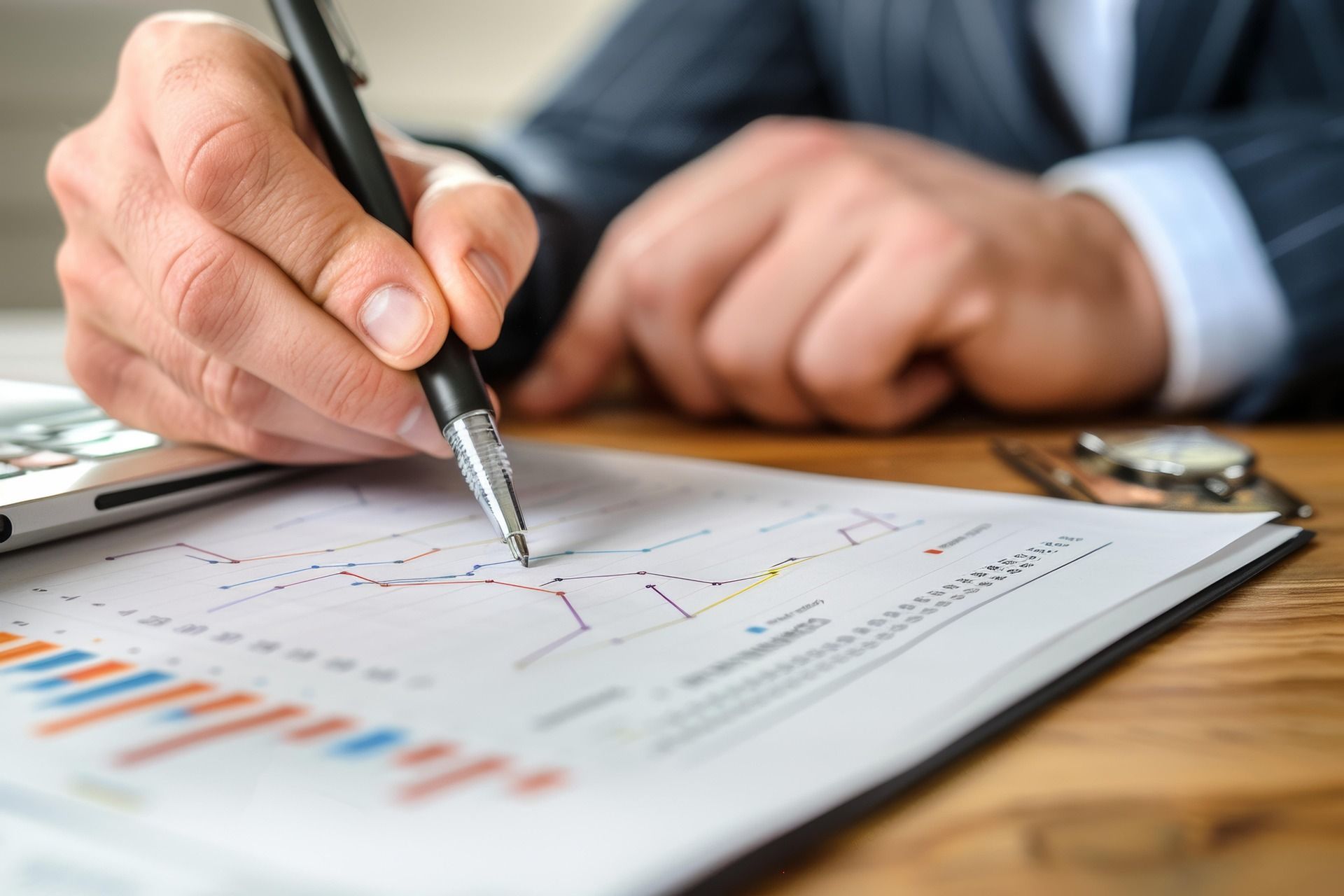 Person in suit writing on financial charts with a pen.