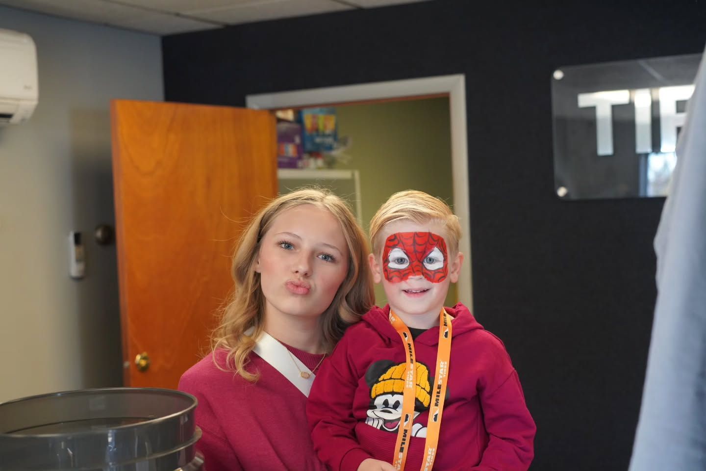 Smiling Young Woman Posing with a Child Wearing Spider-Man Face Paint and a Red Hoodie with a Cartoon Graphic | Tire Tech