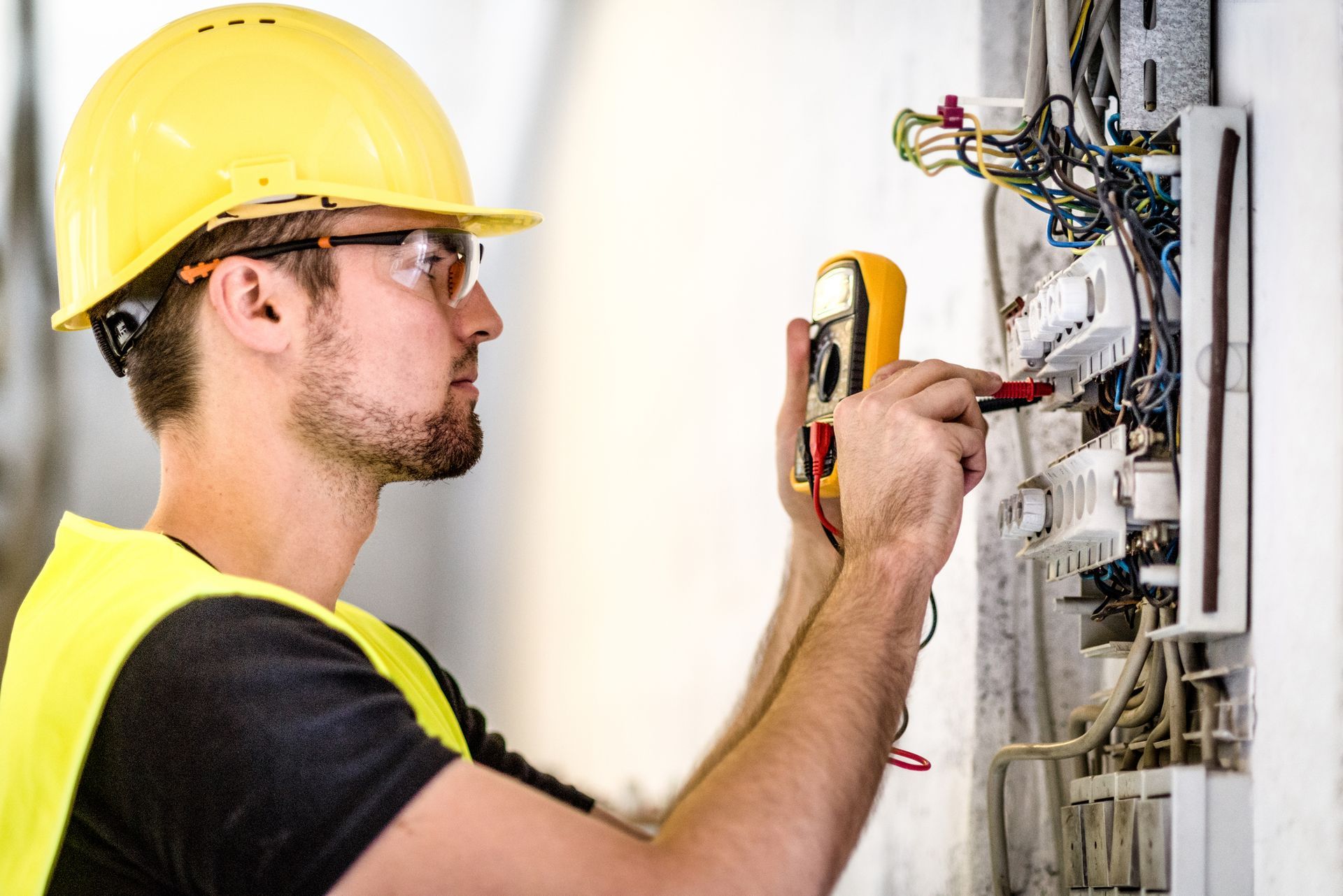 A man wearing a hard hat and safety vest is working on an electrical box.