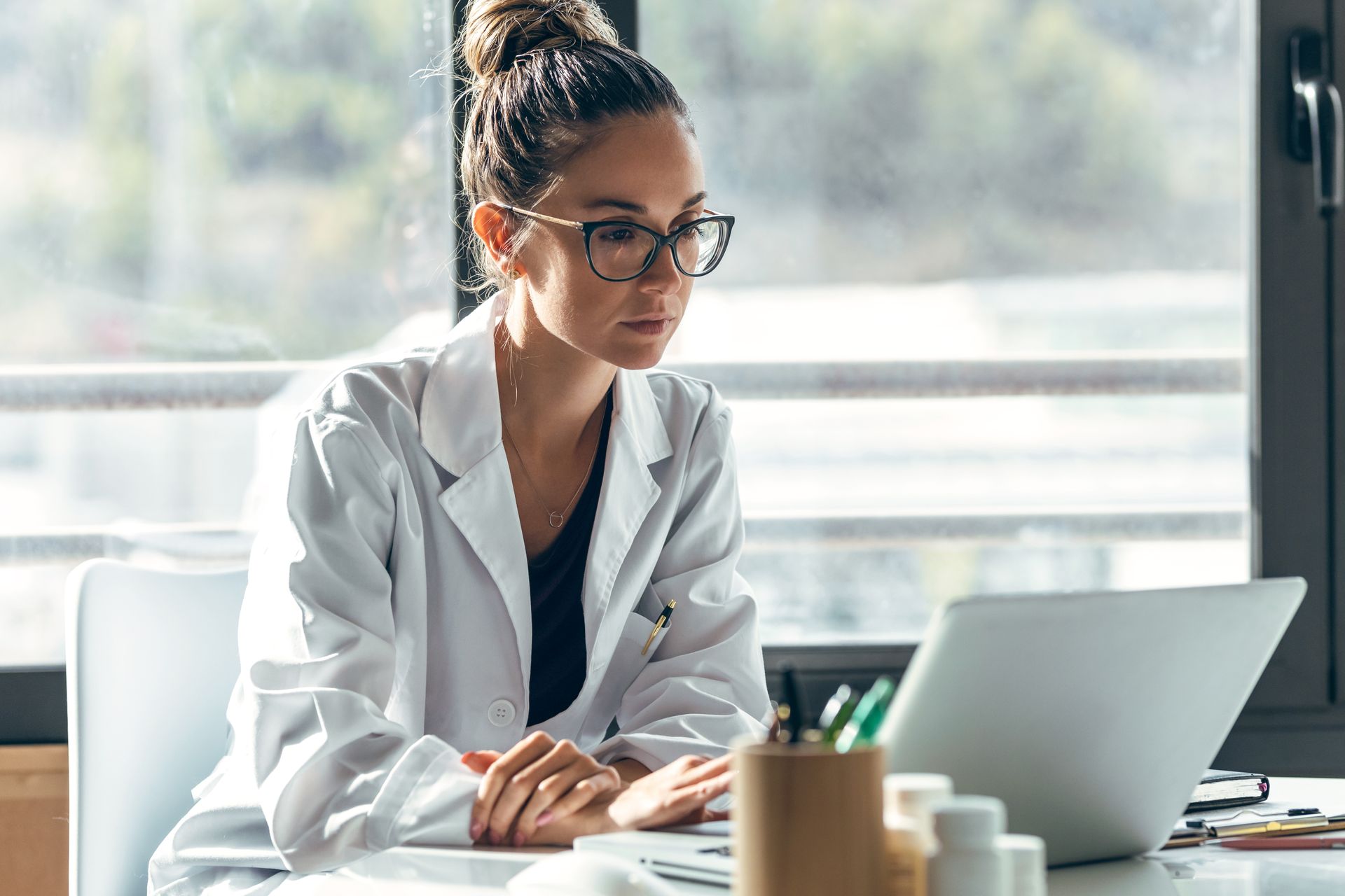 A female doctor is sitting at a desk using a laptop computer.