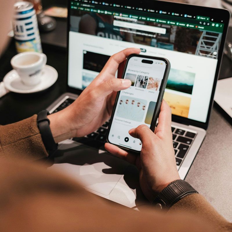 A person is holding a cell phone in front of a laptop