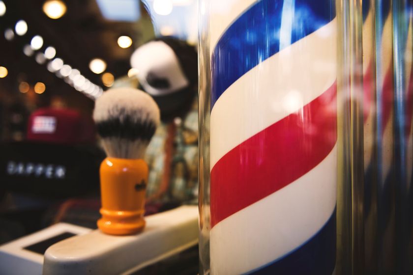 Barber pole with red, white, and blue stripes; shaving brush in front.