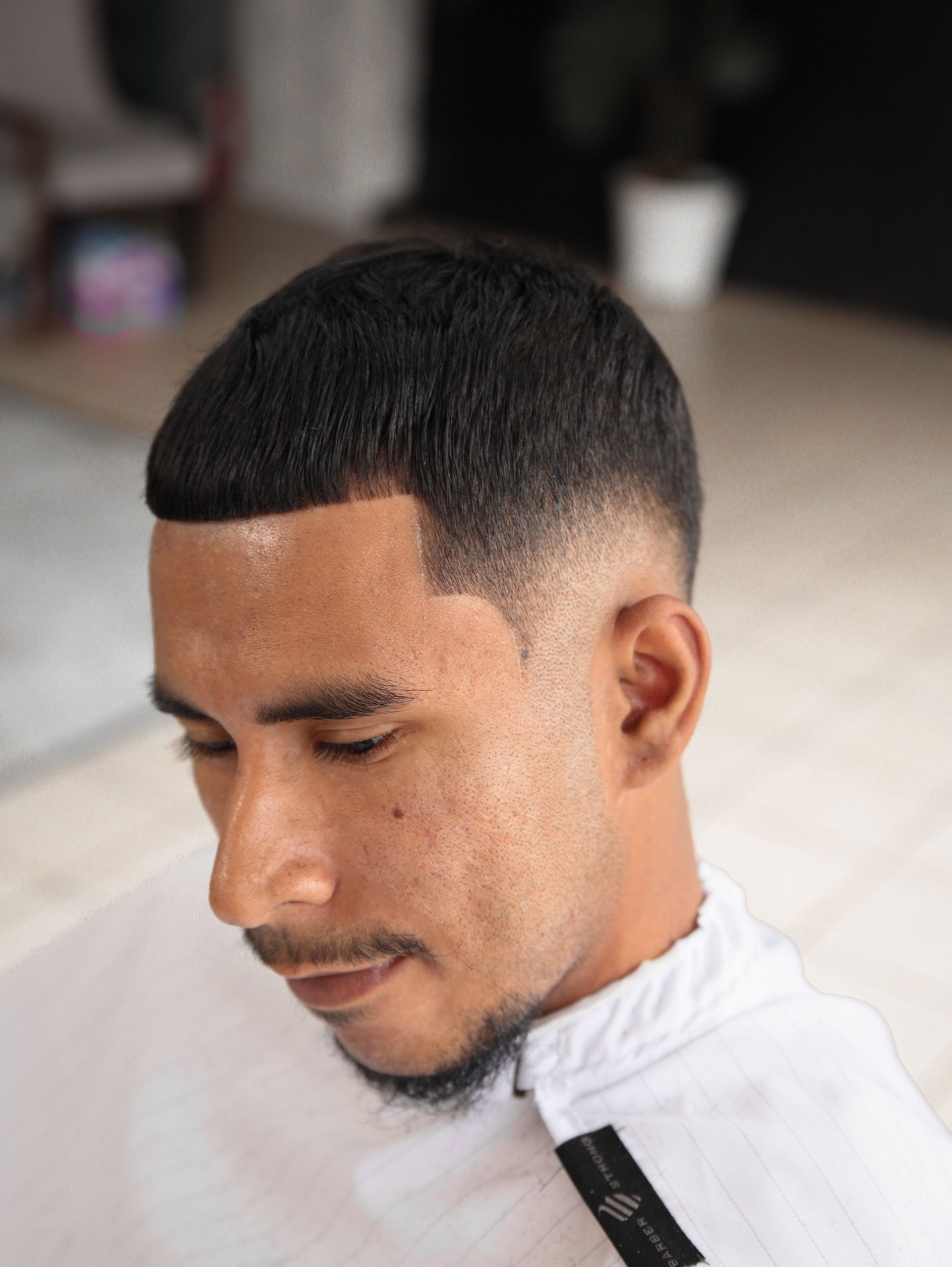 Man with a faded haircut, gazing downward. He wears a white smock.