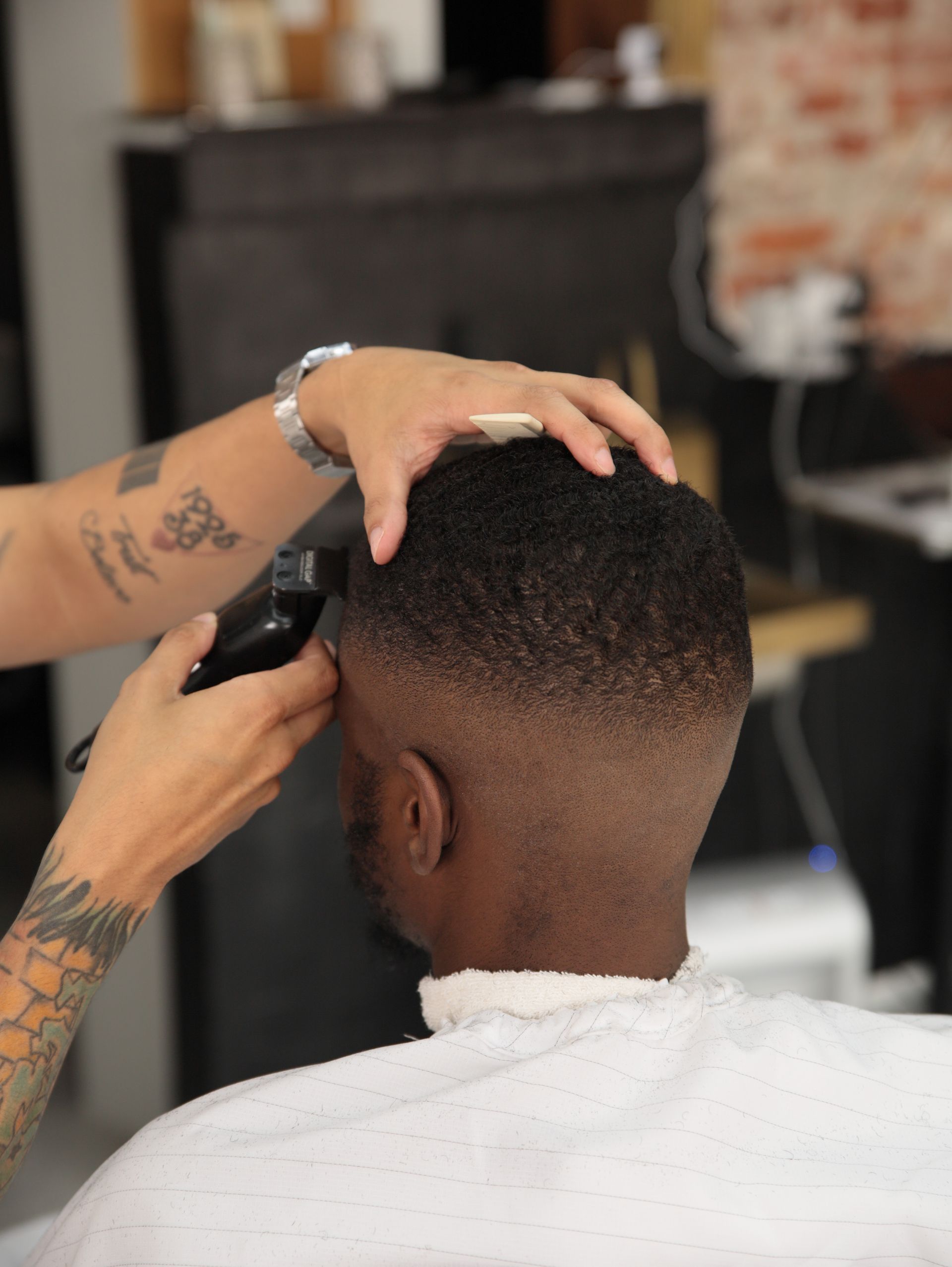 Barber giving a fade haircut, using clippers. The man wears a white barber's cape.