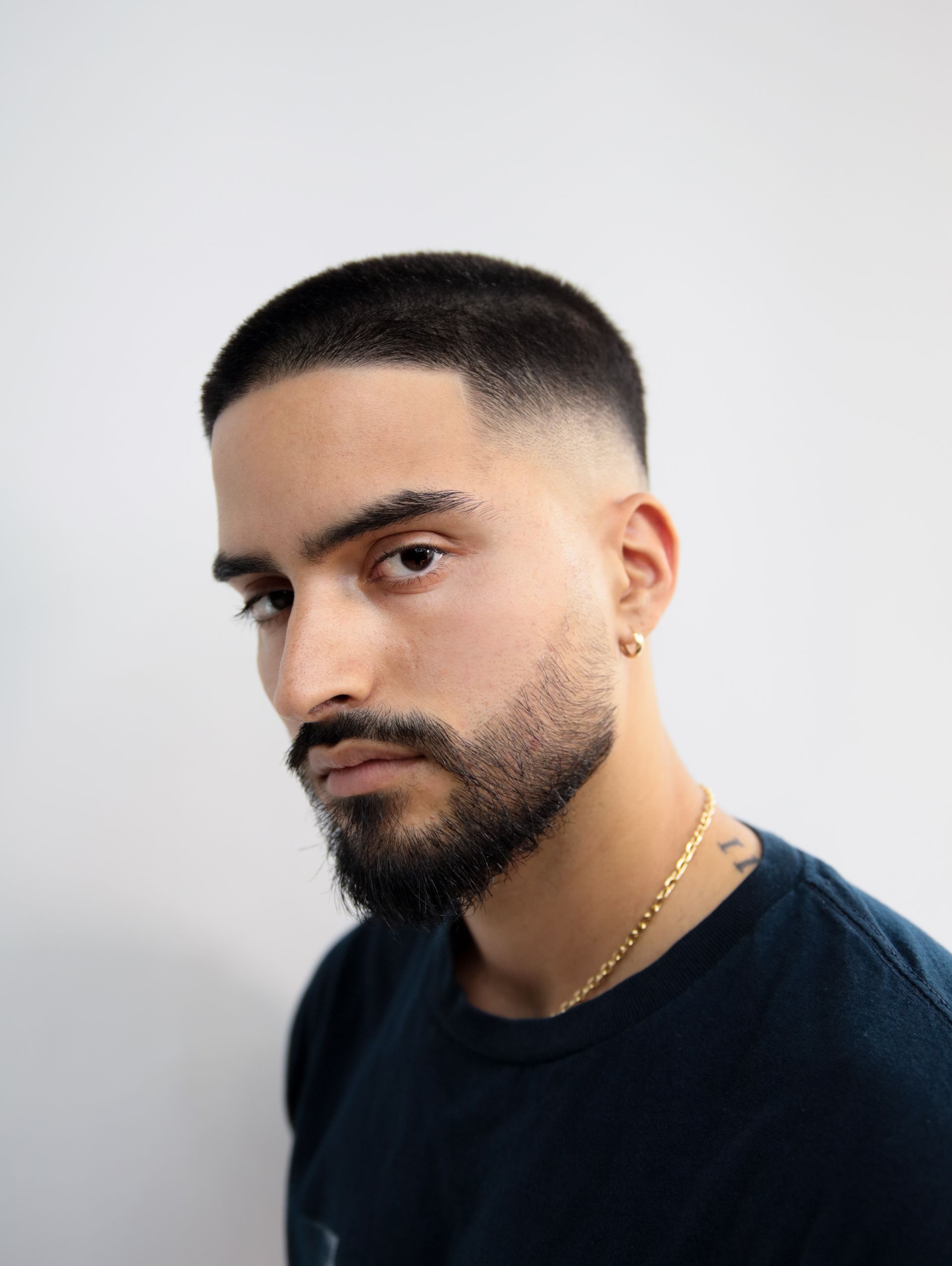 Man with short, faded haircut and beard, wearing a gold chain and earring, looking at the camera.