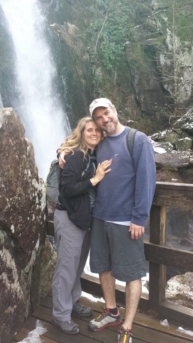A man and a woman are posing for a picture in front of a waterfall.