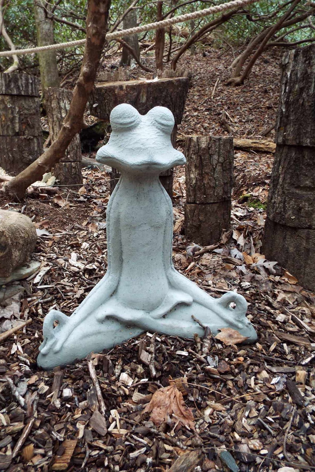 a frog statue is sitting in a lotus position in the woods .