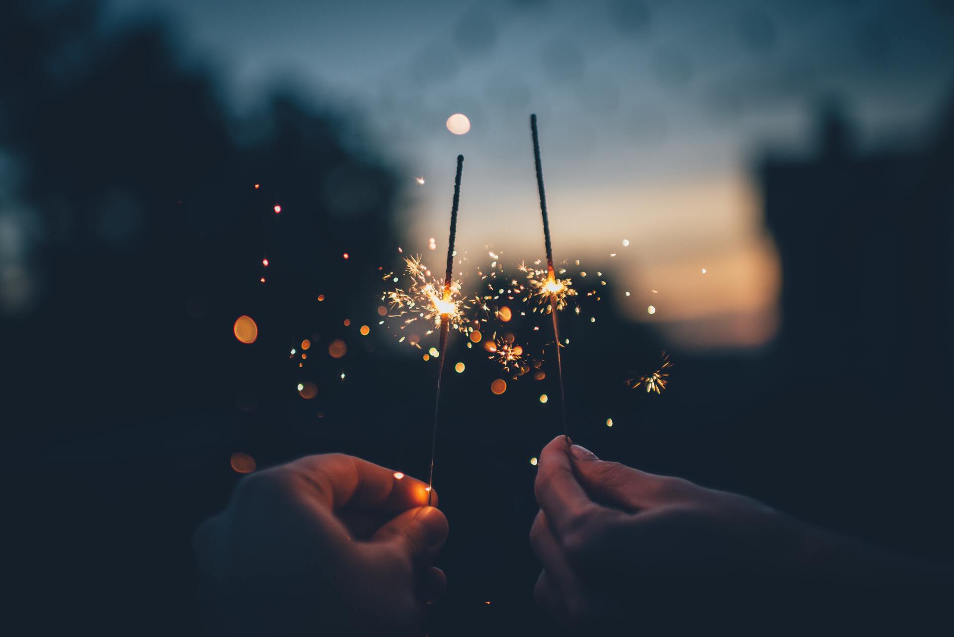 A person is holding two sparklers in their hands at night.