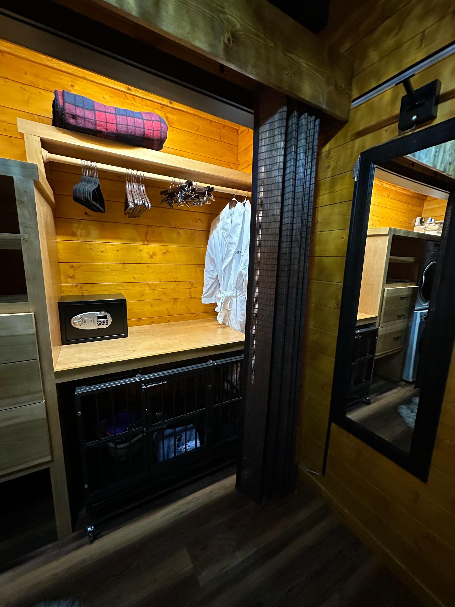 A walk in closet with a dog kennel and a mirror.