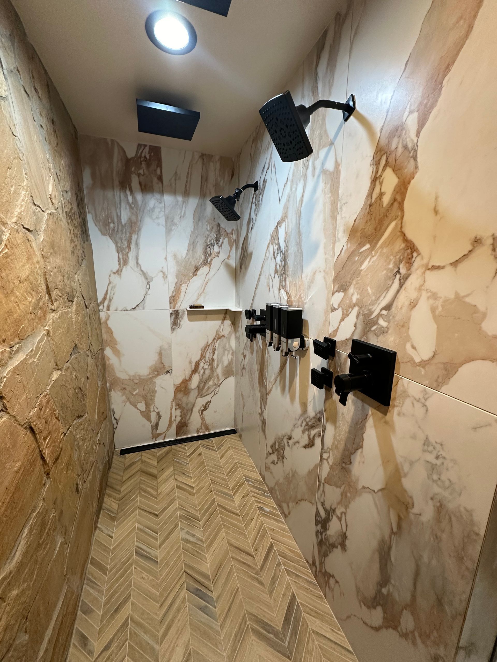 a shower with marble walls and a wooden floor