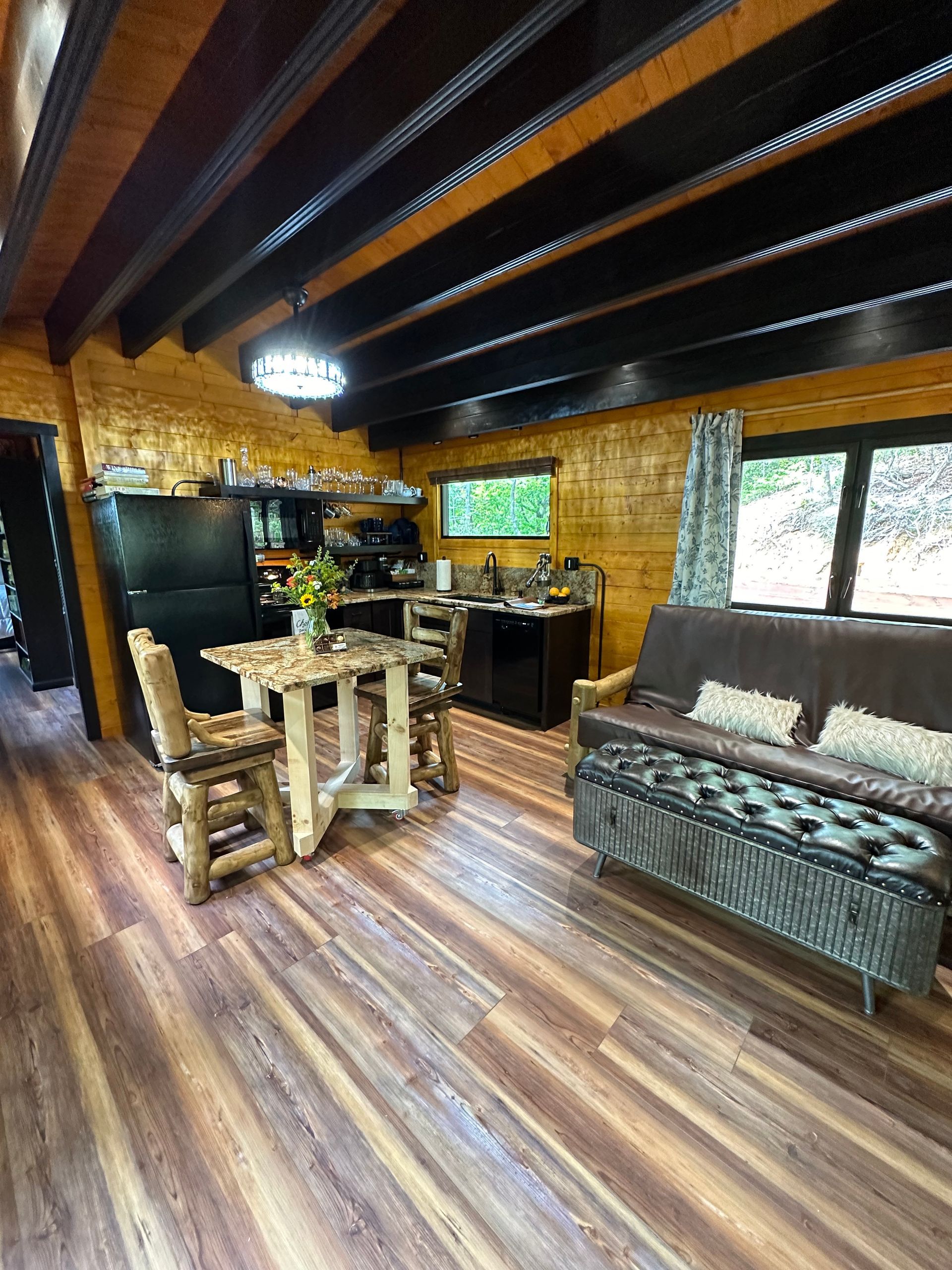 A kitchen in a log cabin with a black refrigerator , stove , sink and dishwasher.