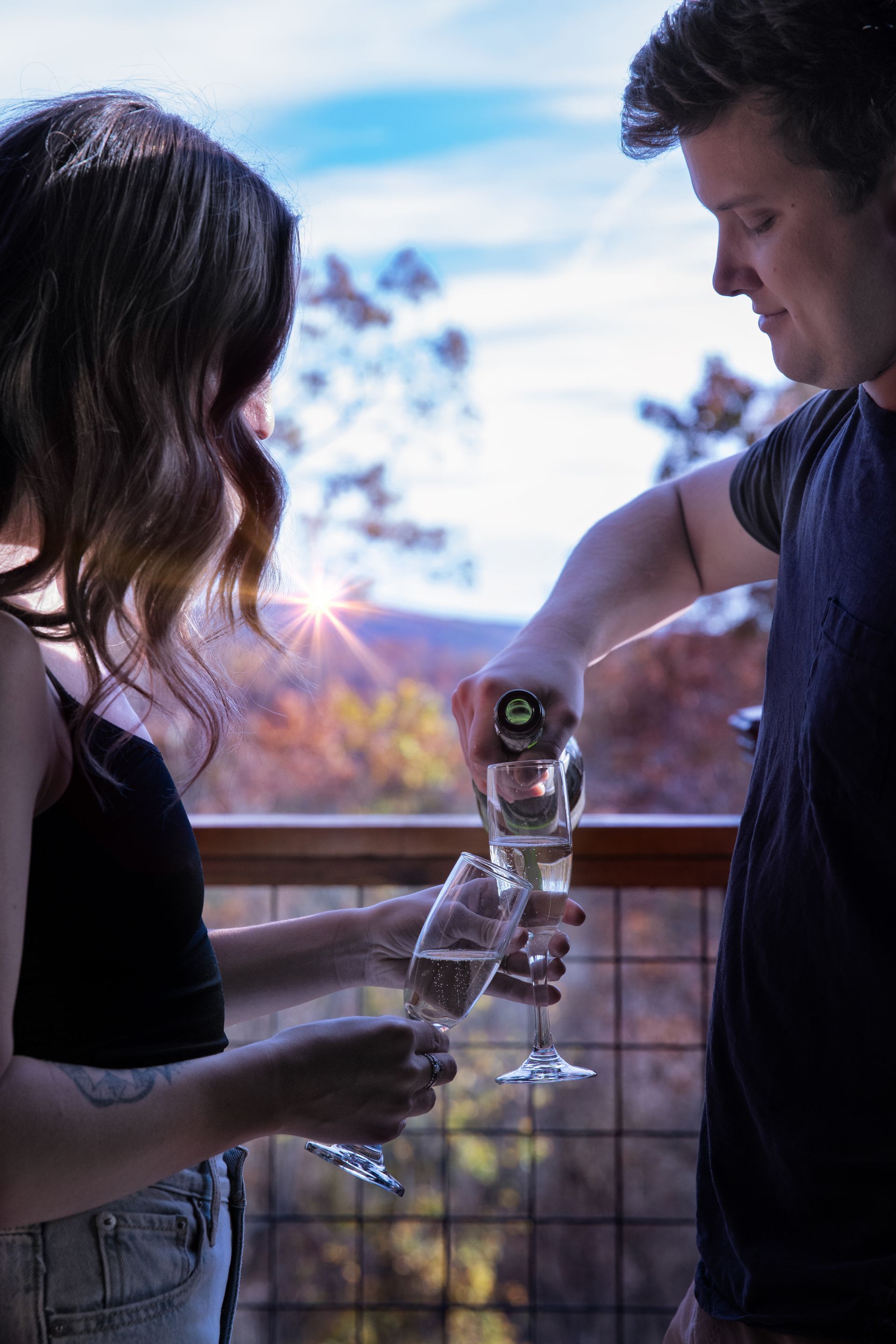Groom dips bride for a kiss on a wooden bridge in a sunlit forest.