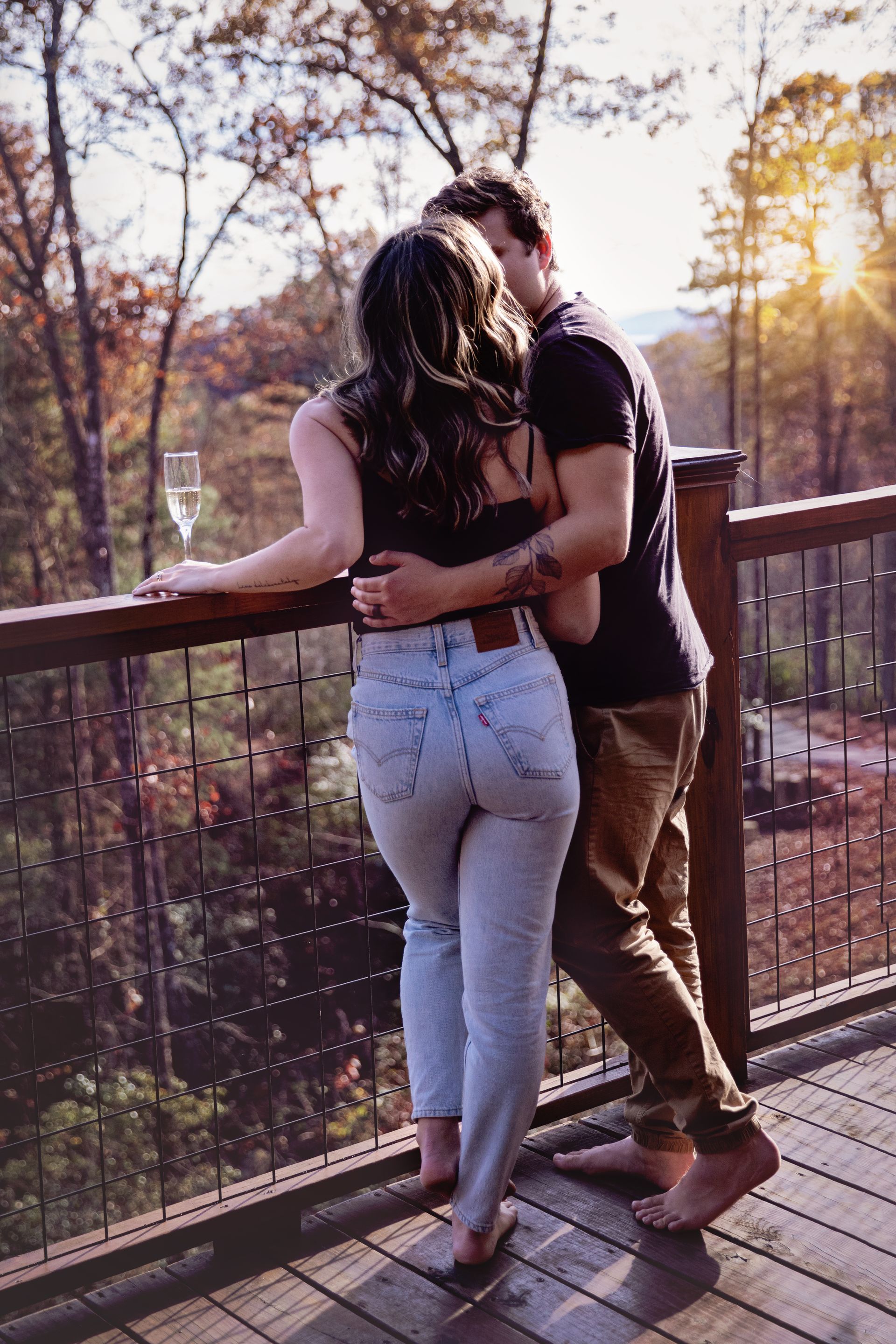 A man and a woman are hugging on a balcony overlooking a forest.