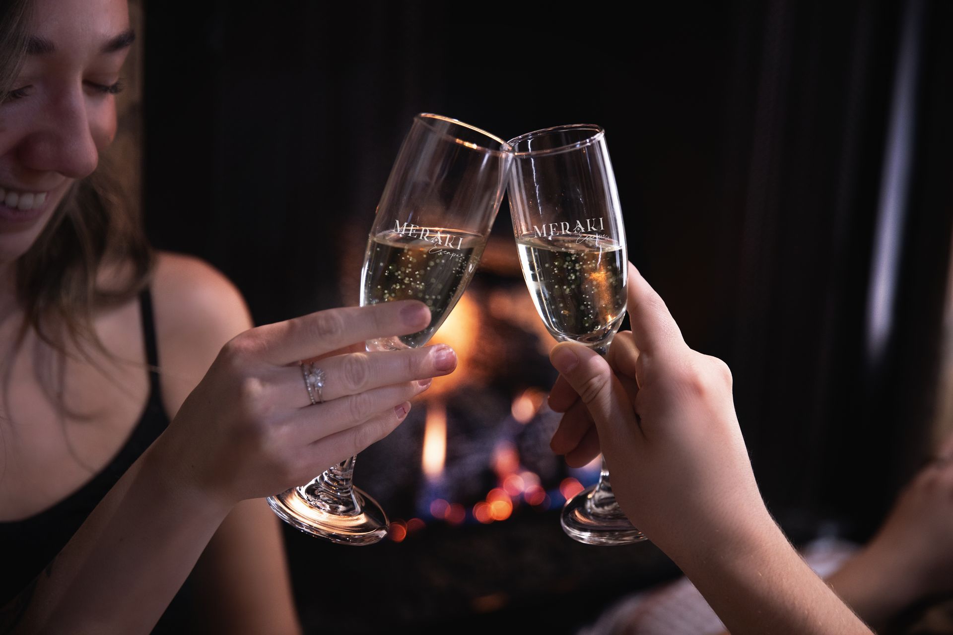 Two women are toasting with champagne in front of a fireplace.