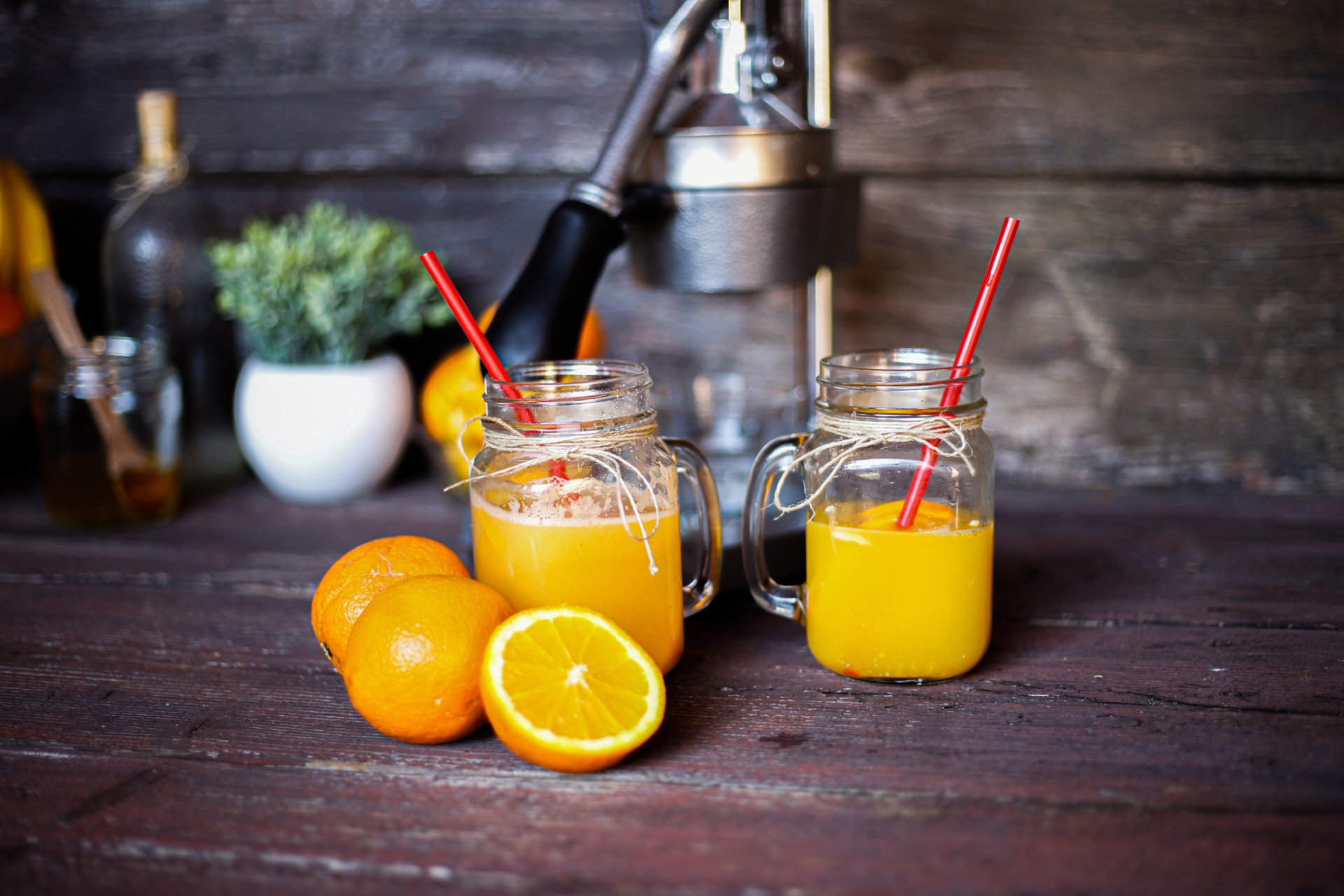 Two mason jars filled with orange juice and oranges on a wooden table.