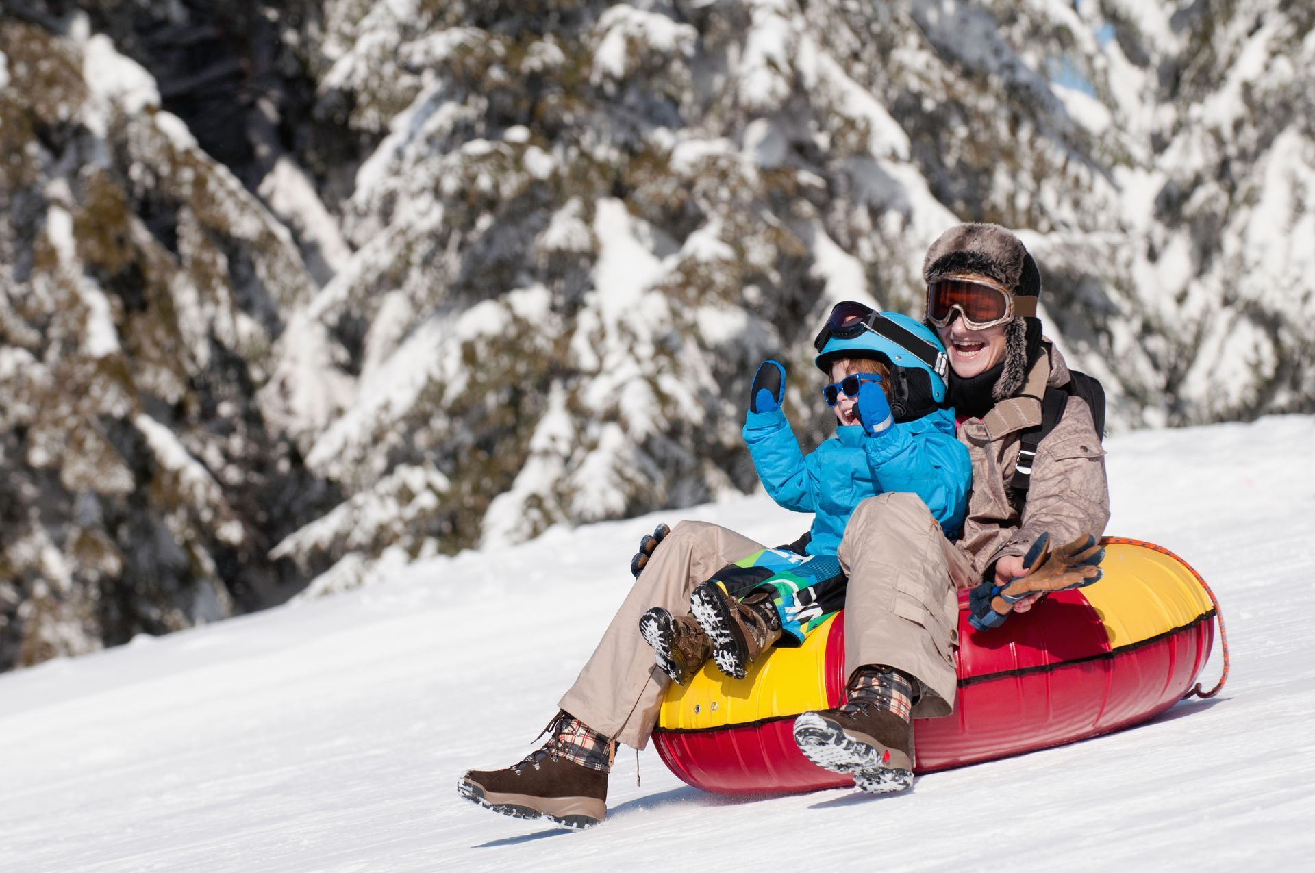 A man and a child are riding a snow tube down a snow covered hill.