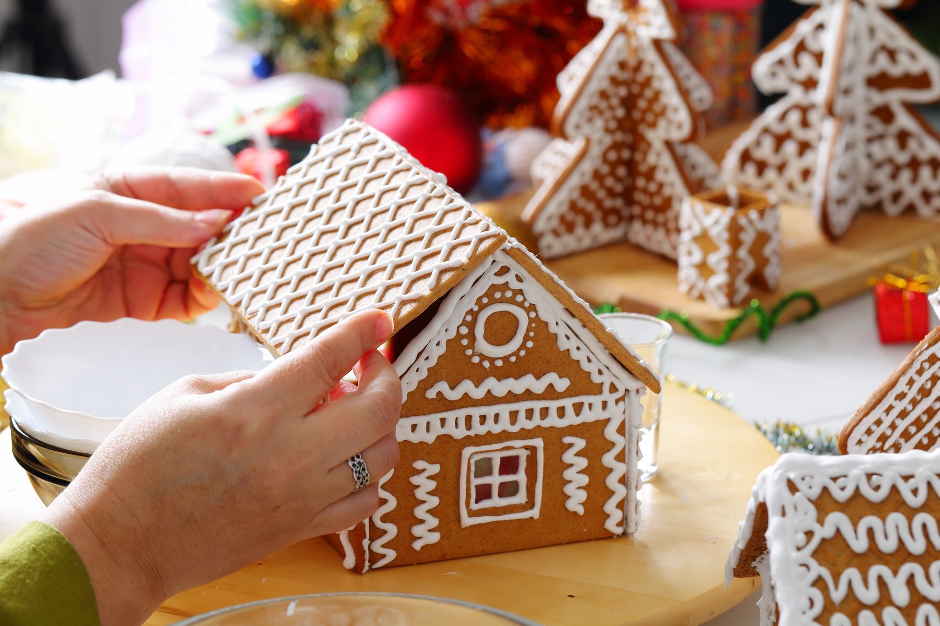 A person is decorating a gingerbread house with white frosting.