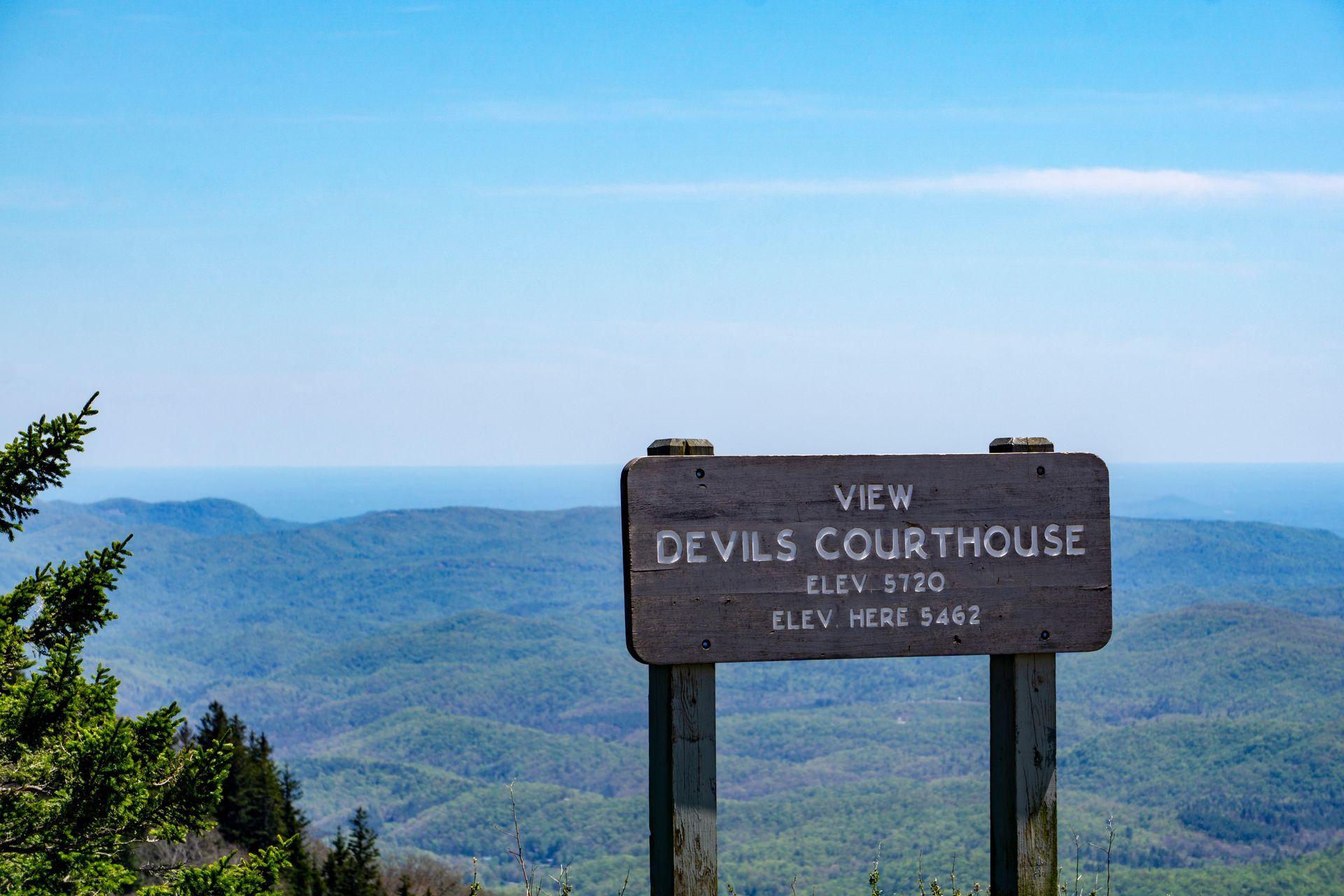 A wooden sign on top of a mountain with a view of the devil 's courthouse.