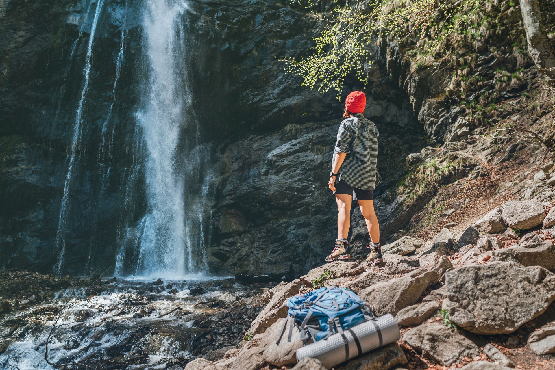 A person with a backpack is standing in front of a waterfall.