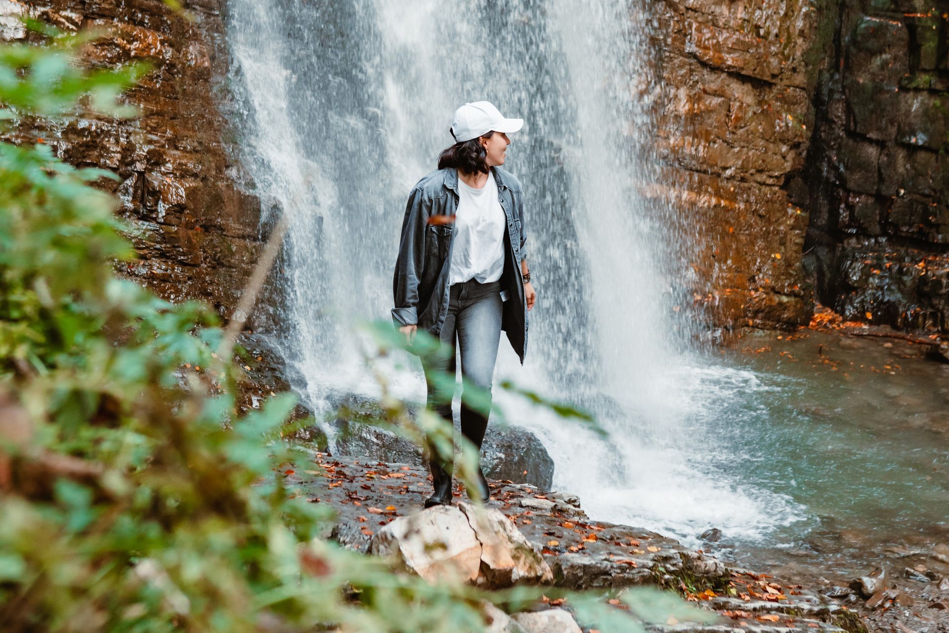 A woman is standing in front of a waterfall.