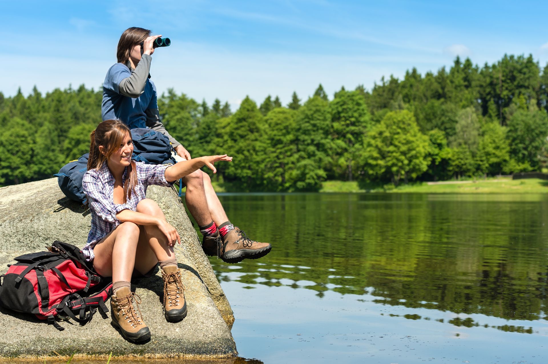 A man and a woman are sitting on a rock near a lake.