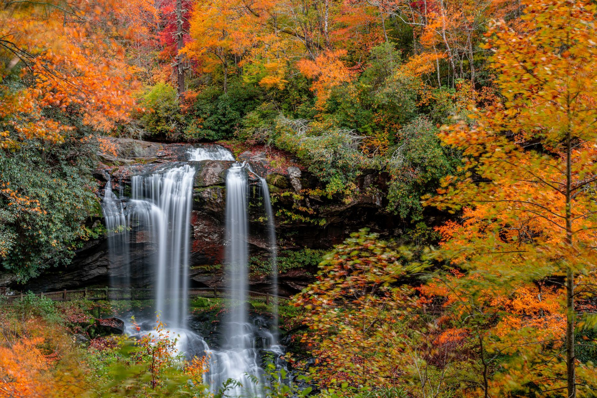 A waterfall in the middle of a forest surrounded by trees with autumn leaves.