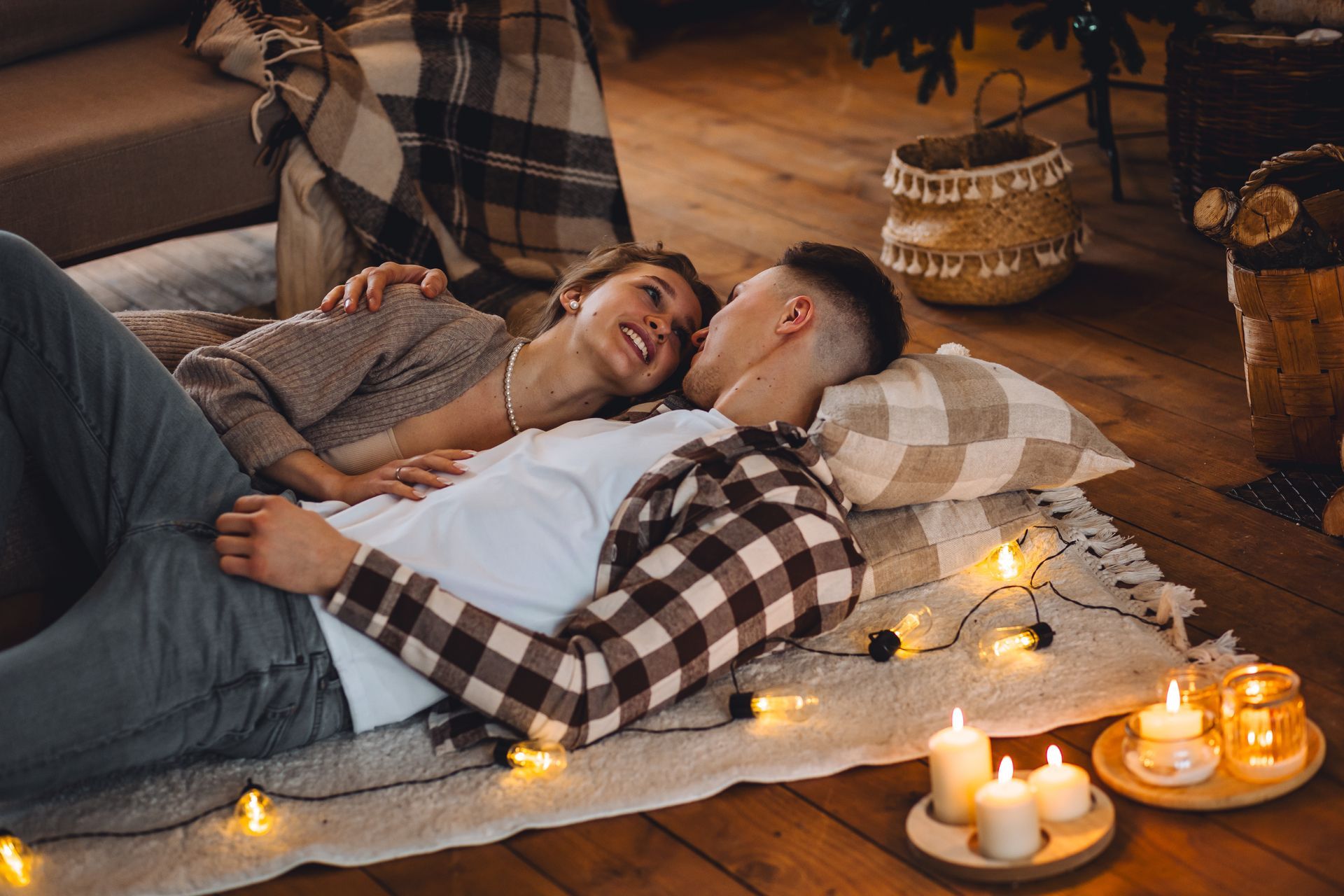 A man and a woman are laying on a blanket on the floor next to candles.