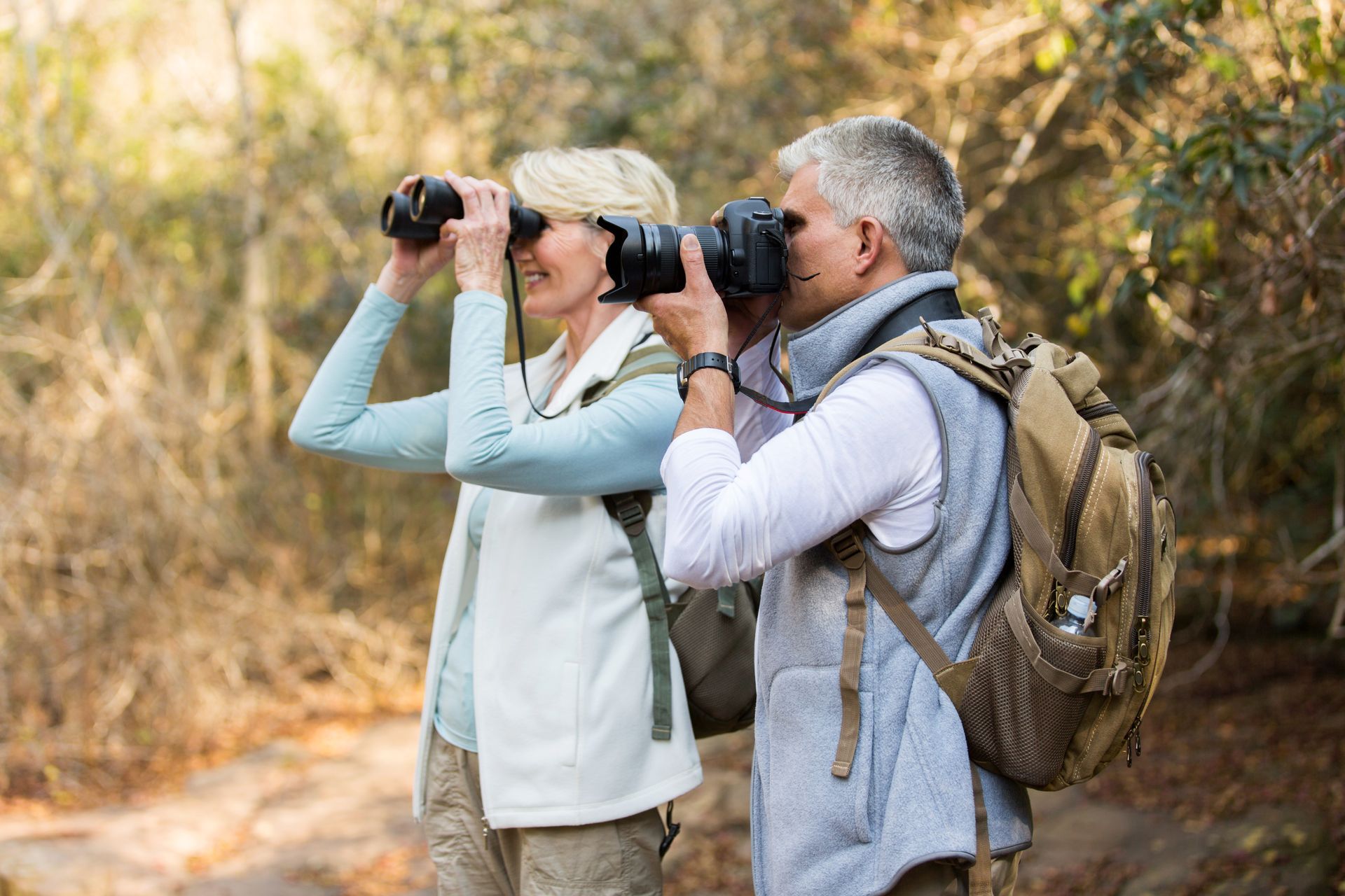 A man and a woman are looking through binoculars in the woods.